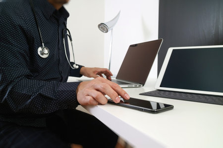 smart medical doctor working with smart phone and digital tablet and laptop computer and stethoscope on wood desk in modern officeの写真素材