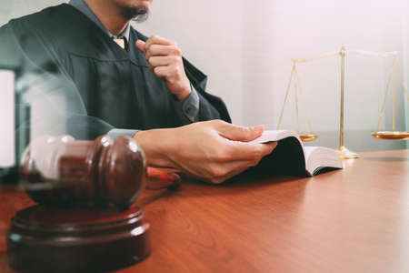 justice and law concept.Male judge in a courtroom with the gavel,opening holy book and digital tablet computer with brass scale on wood tableの写真素材