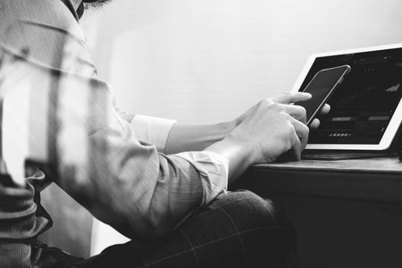 success businessman hand using smart phone,digital tablet docking smart keyboard on wood desk,black...