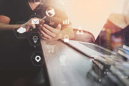 businessman working with smart phone and laptop computer on wooden desk in modern office with virtual icons interfaceの写真素材