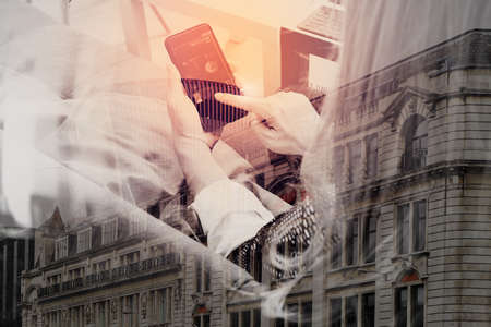 brunette woman using smart phone and digital tablet computer on sofa in living room with London city Exposureの写真素材