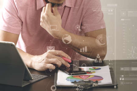 businessman in pink t-shirt working with smart phone and digitl tablet computer and document on wooden desk in modern office with virtual icon diagramの写真素材