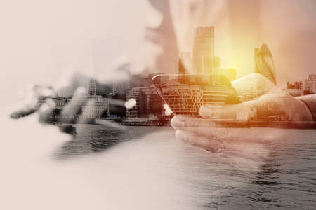 close up of smart medical doctor working with mobile phone and stethoscope on dark wooden desk with London city exposureの写真素材