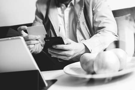 hipster hand using smart phone,digital tablet docking keyboard,holding cradit card payments online business,sitting on sofa in living room,work at home concept,black and whiteの写真素材