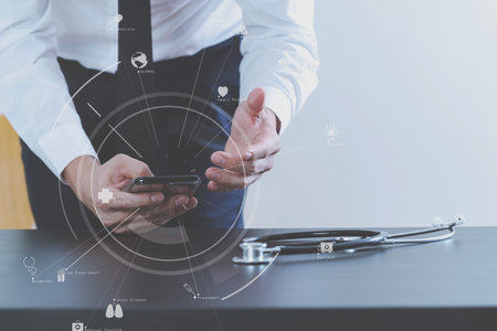 close up of smart medical doctor working with smart phone and stethoscope on dark wooden desk with virtual icon diagramの写真素材