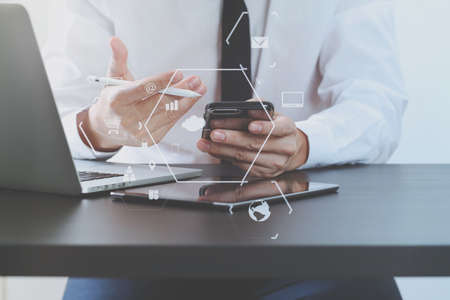 close up of businessman working with mobile phone on wooden desk in modern office with virtual icon diagramの写真素材