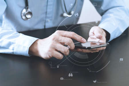 close up of smart medical doctor working with smart phone and stethoscope on dark wooden desk with virtual icon diagramの写真素材