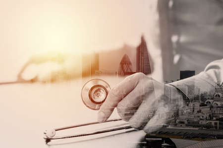 close up of smart medical doctor working with stethoscope and mobile phone on dark wooden desk in modern hospital with London city exposureの写真素材