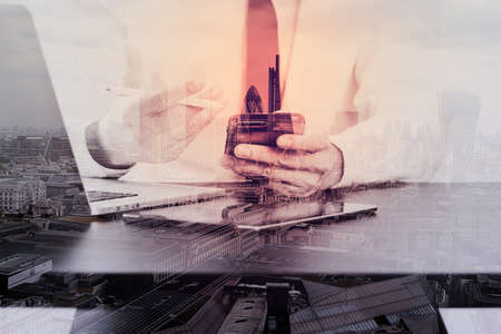 close up of businessman working with smart phone and digital tablet and laptop computer  on wooden desk in modern office with London city exposureの写真素材