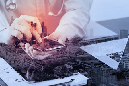 smart medical doctor working with smart phone and stethoscope and laptop and digital tablet computer on dark wooden desk with London city exposureの写真素材