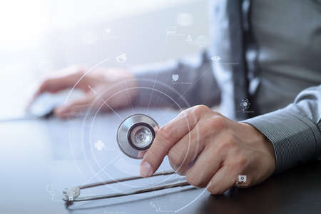 close up of smart medical doctor working with stethoscope and mobile phone on dark wooden desk in modern hospital with virtual reality icon diagramの写真素材