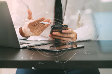 Hands of businessman using mobile phone in modern office with laptop and digital tablet computer with VR icon diagramの写真素材