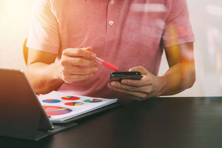 businessman in pink t-shirt working with smart phone and digitl tablet computer on wooden desk in modern office with glass reflected viewの写真素材