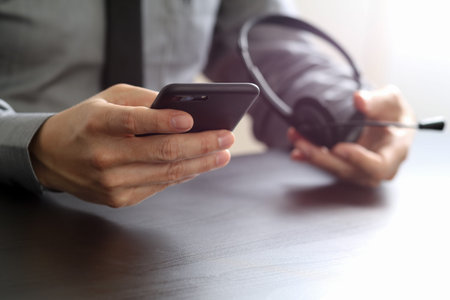 businessman using VOIP headset with mobile phone and concept communication call center on wooden deskの写真素材
