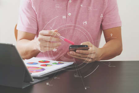 businessman in pink t-shirt working with mobile phone and digitl tablet computer and document on wooden desk in modern office with virtual icon diagramの写真素材