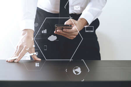close up of businessman working with smart phone on wooden desk in modern office with virtual icon diagramの写真素材