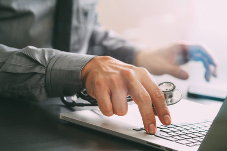 close up of smart medical doctor working with laptop computer and stethoscope on dark wooden deskの写真素材