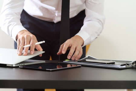 close up of businessman working with smart phone and digital tablet and laptop computer on wooden desk in modern officeの写真素材