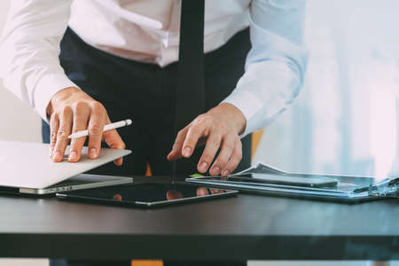 close up of businessman working with smart phone and digital tablet and laptop computer on wooden desk in modern office with glass reflected view close up of businessman working with smart phone and digital tablet and laptop computer on wooden desk in modern office with glass reflected view