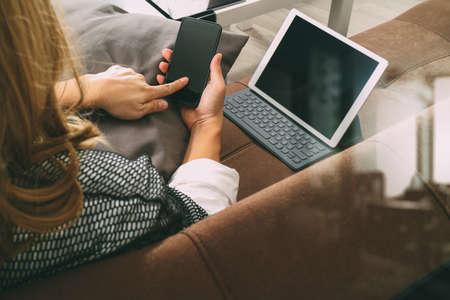 brunette woman using smart phone and digital tablet computer on sofa in living roomの写真素材