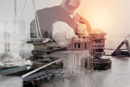 Double exposure of justice and law concept.Male judge in a courtroom with the gavel,working with smart phone and digital tablet computer with brass scale on wood table with London cityの写真素材