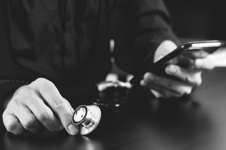 close up of smart medical doctor working with smart phone and stethoscope on dark wooden desk,black...