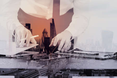 close up of businessman working with smart phone and digital tablet and laptop computer on wooden desk in modern office with London city exposureの写真素材