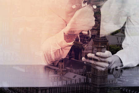 close up of businessman working with smart phone on wooden desk in modern office with London city exposureの写真素材