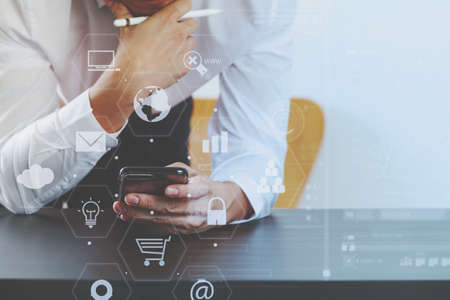 close up of businessman working with smart phone on wooden desk in modern office with virtual icon diagramの写真素材