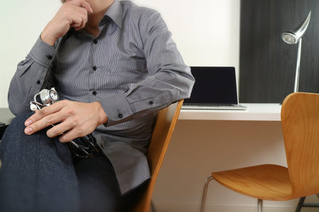 smart medical doctor holding stethoscope and thinking with laptop computer on dark wooden desk in modern officeの写真素材