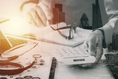 Healthcare costs and fees concept.Hand of smart doctor used a calculator for medical costs in modern hospital with buildings exposureの写真素材