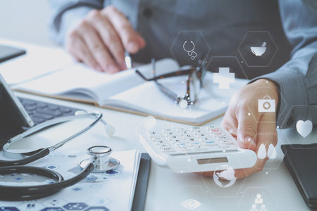 Healthcare costs and fees concept.Hand of smart doctor used a calculator for medical costs in modern hospital with VR icon diagramの写真素材