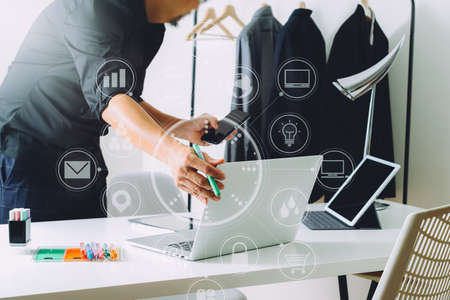 Fashion designer working with mobile phone and using laptop with digital tablet computer in modern studio with VR icon diagramの写真素材