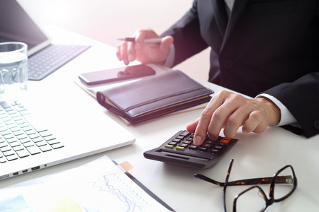 businessman hand working with finances about cost and calculator and latop with mobile phone on...