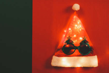 Greeting Season concept.Santa Claus hat with star light and glasses that decoration with Christmas tree on red and green backgroundの写真素材