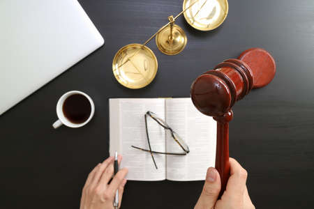 justice and law concept.Top view of Male judge hand in a courtroom with the gavel and brass scale and computer and open bible book on dark wood tableの写真素材