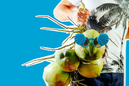Summer and holiday fashion collage magazine concept.Man Wearing palm trees graphics on T-shirt and holding cluster of coconuts with items on blue backgroundの写真素材
