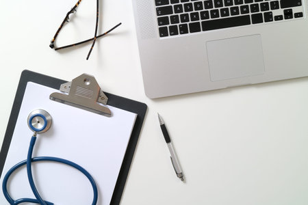 blank stethoscope and gray clipboard and eyeglasses and laptop computer on white desk background