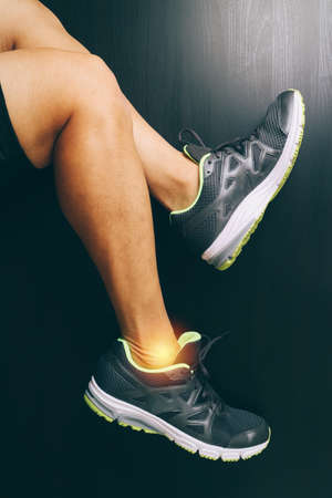 Runner sportsman holding ankle in pain with Broken twisted joint running sport injury and Athletic man touching foot due to sprain on dark backgroundの写真素材