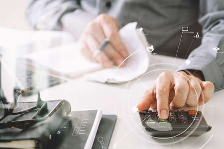 businessman hand working with finances about cost and calculator and latop with mobile phone on withe desk in modern office with VR icon diagramの写真素材
