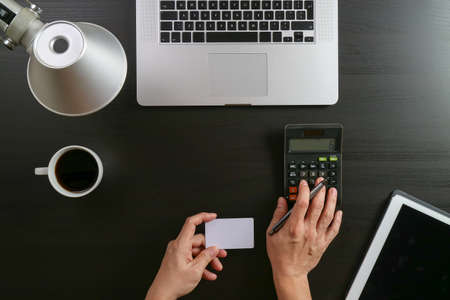 Internet shopping concept.Top view of hands working with calculator and laptop and credit card and tablet computer on dark wooden table backgroundの写真素材