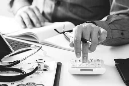 Healthcare costs and fees concept.Hand of smart doctor used a calculator for medical costs in modern hospital,black and whiteの写真素材