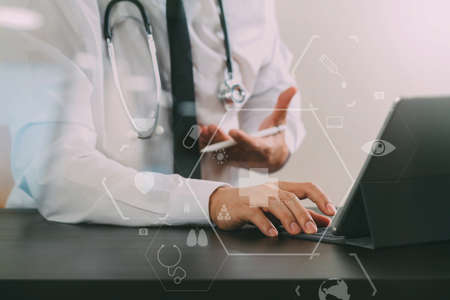 Close up of smart medical doctor working with digital tablet computer and stylus pen and stethoscope on dark wooden desk with virtual icon diagramの写真素材