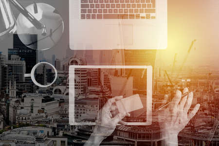 Internet shopping concept.Top view of hands working with calculator and laptop and credit card and tablet computer on dark wooden table background with buildings exposureの写真素材