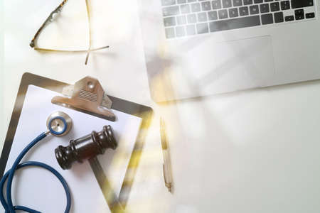 Dark Gavel With Medical Stethoscope near Laptop on white desk In Courtroom conceptの写真素材