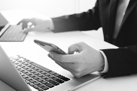 Hands of businessman using mobile phone in modern office with laptop and digital tablet computer...