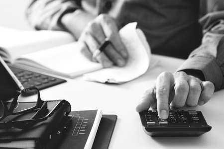 businessman hand working with finances about cost and calculator and latop with mobile phone on withe desk in modern office,black and whiteの写真素材