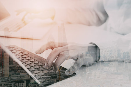 close up of businessman typing keyboard with laptop computer and digital tablet on white desk in...