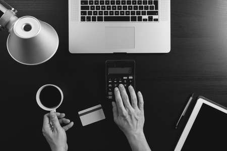 Internet shopping concept.Top view of hands working with calculator and laptop and credit card and tablet computer on dark wooden table background,black and whiteの写真素材