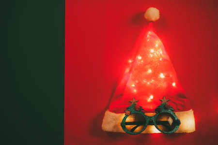 Greeting Season concept.Santa Claus hat with star light and glasses that decoration with Christmas tree on red and green backgroundの写真素材
